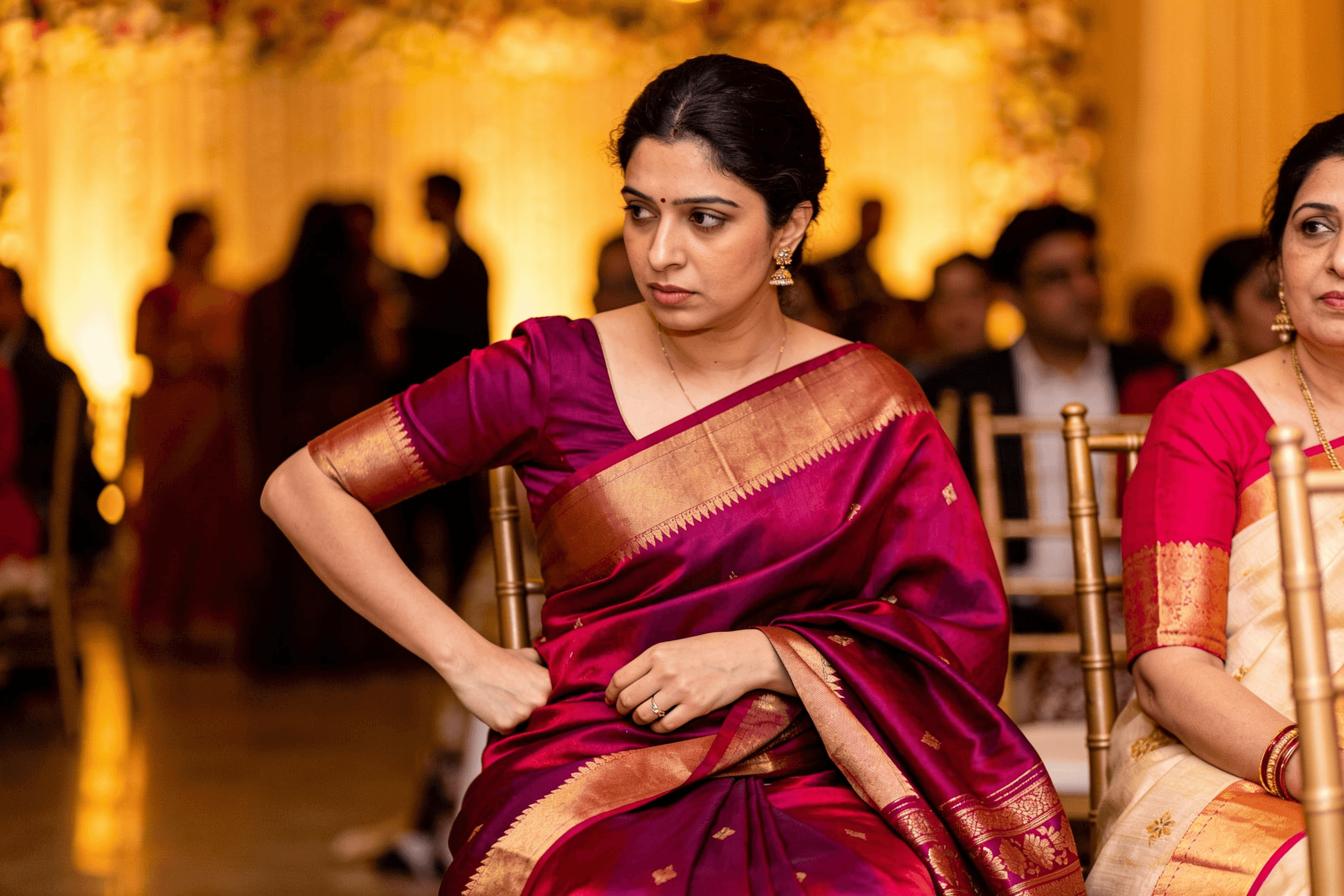 Woman seated at a function in a Kanchipuram silk saree, adjusting the drape at her waist