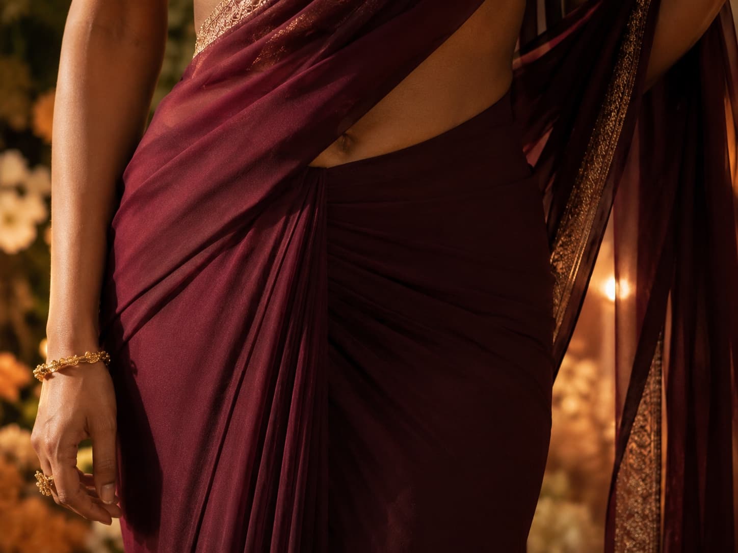 Close view of a maroon georgette saree draping smoothly at the waist under warm reception lighting, gold bangles at the wrist — illustrating the fabric and occasion context this guide covers